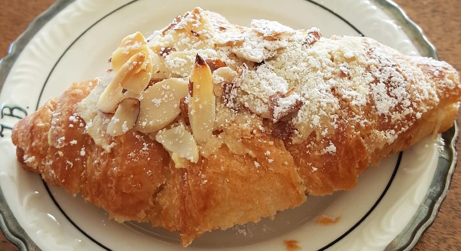 Golden brown almond croissant dusted with powdered sugar on a round white plate