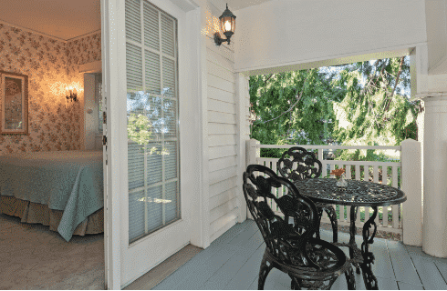 Outdoor covered deck with black table and two chairs and French doors open into a guestroom