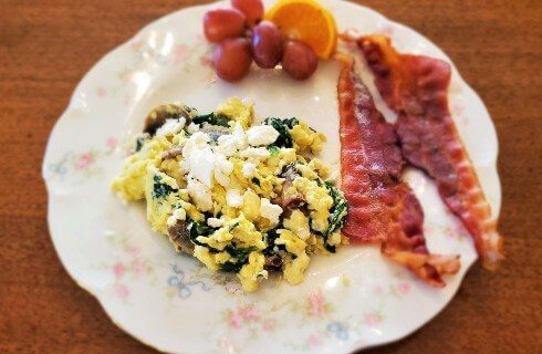 Round white plate with egg scramble two pieces of bacon and grapes