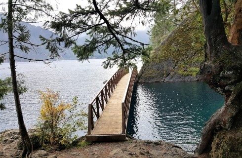 Small bridge over a body of water with trees and a mountain range in the distance