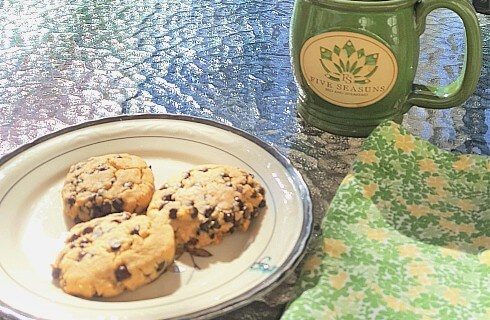 Small round plate with three homemade cookies on a table with a green ceramic mug
