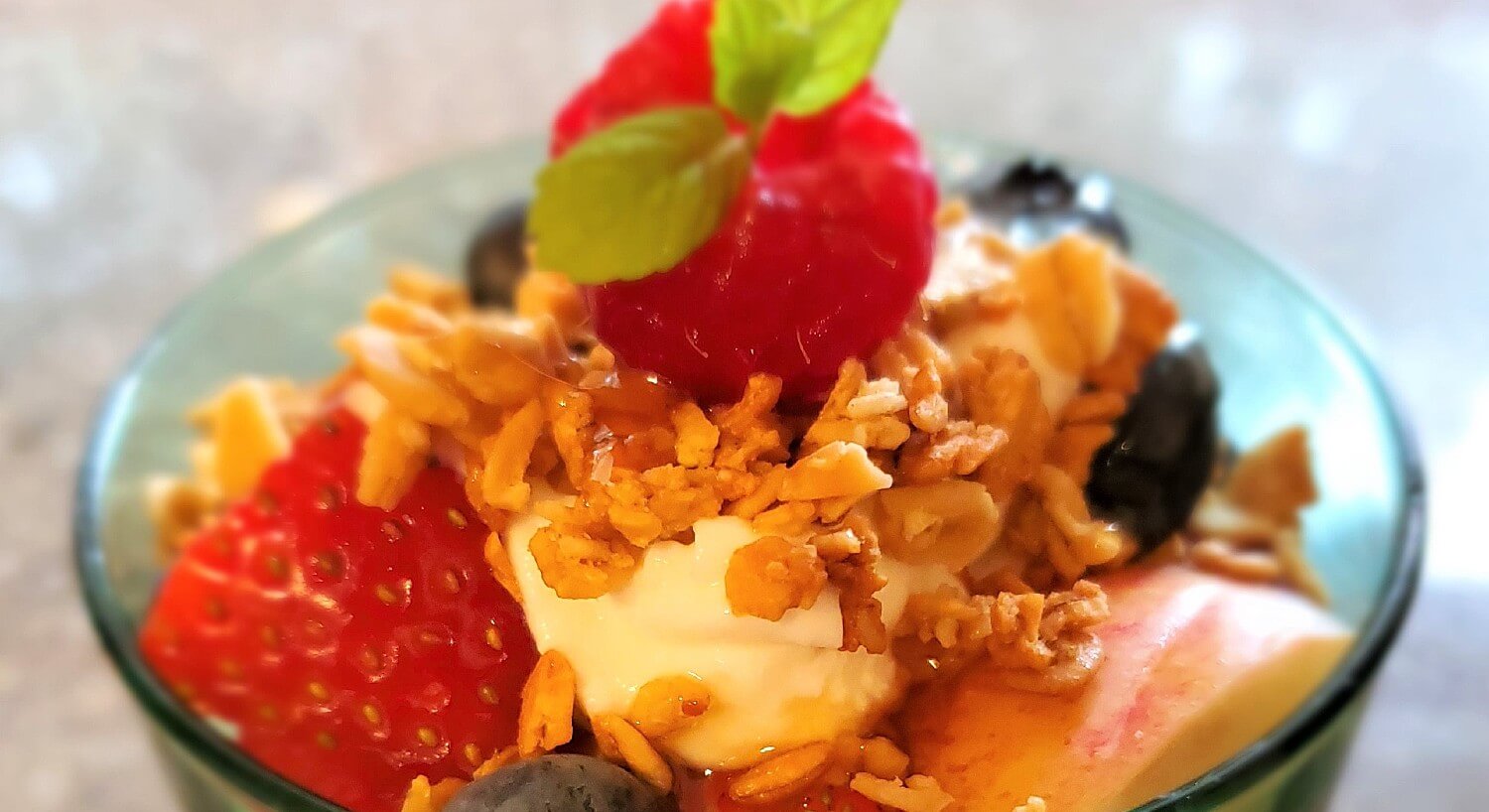 Glass dish filled with fruit, yogurt and topped with golden brown granola 