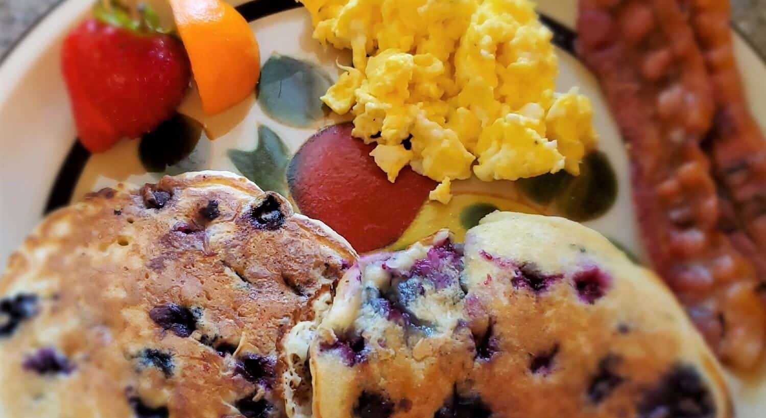 Breakfast plate with two blueberry pancakes, bacon, eggs and fruit 