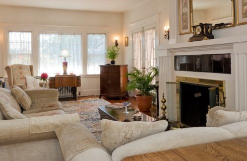 Beautiful white living room with couch and loveseat, fireplace with large mantle, bright windows and French doors