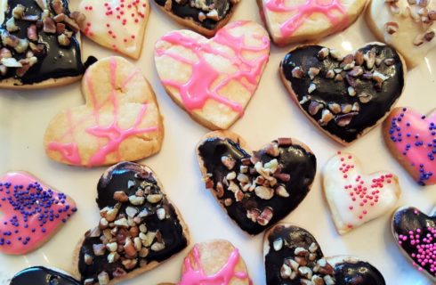 Heart shaped cookies with chocolate and pink frosting and sprinkles on a white platter