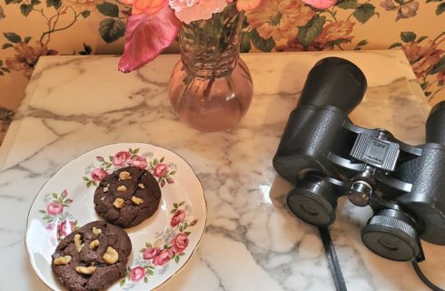 Marble side table holding round plate of chocolate cookies, binoculars and vase of flowers