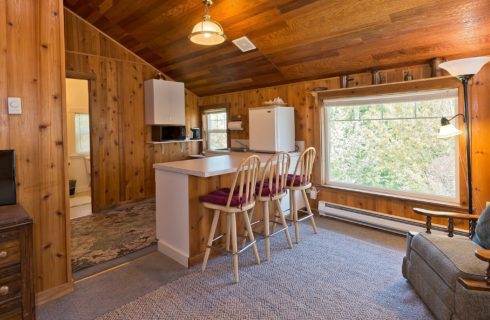 Kitchenette area of a home with large window showing trees and upholstered sitting chair