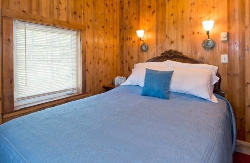 Guest room with wood paneled walls, queen bed with blue quilt and large window