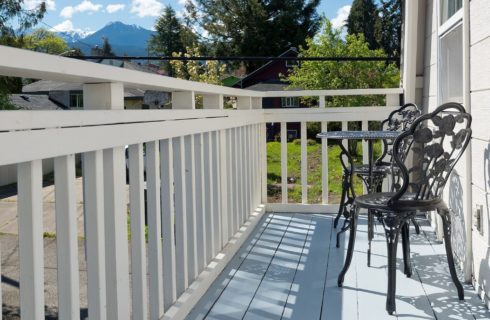 Outside patio with white railings, wrought iron table with two chairs and mountain range in the distance