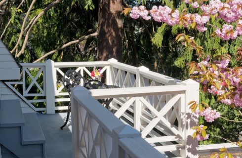 Outdoor patio area with table and two chairs and white railing surrounded by trees and bushes with pink flowers