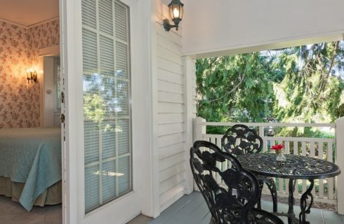 Outside patio with iron table and two chairs with French doors open into a guest room with a king bed