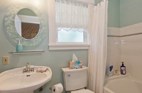 Bathroom with light green walls, pedestal sink, toilet, tiled shower with tub and one window