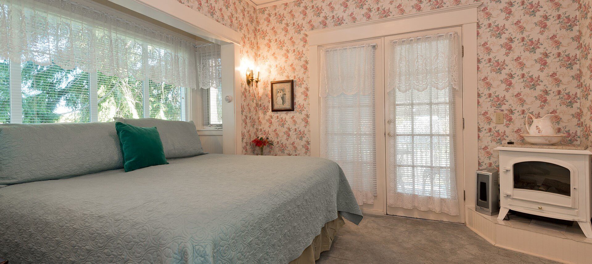 Elegant guest room with king bed, white electric fireplace, bright windows and French doors with lace curtains