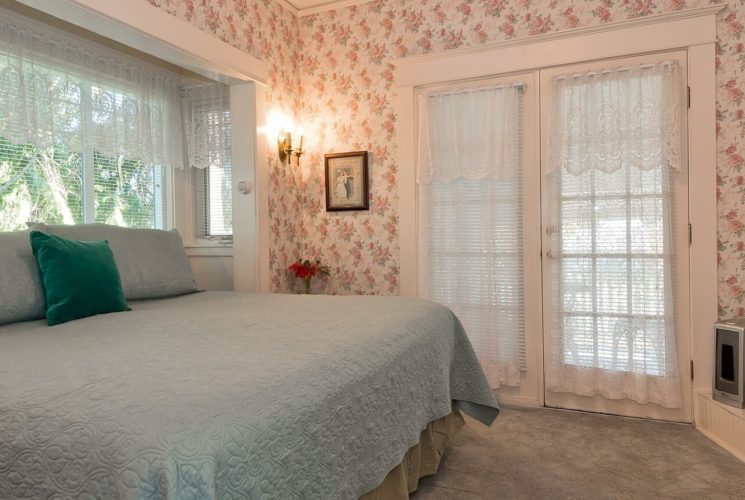 Elegant guest room with king bed, white electric fireplace, bright windows and French doors with lace curtains