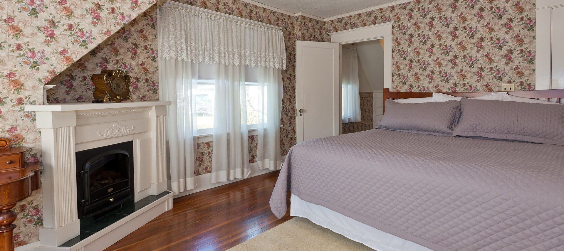 Spacious suite with king bed, fireplace with white mantle, hardwood floors and bright windows