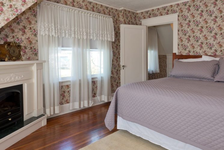 Spacious suite with king bed, fireplace with white mantle, hardwood floors and bright windows