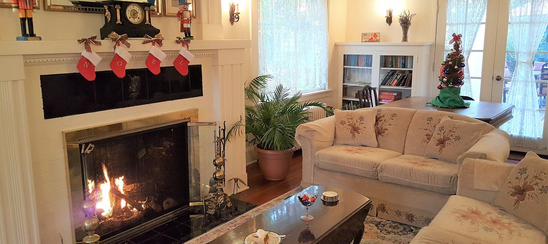 Cozy living room with two couches and coffee table in front of a lit fireplace with mantle holding small stockings