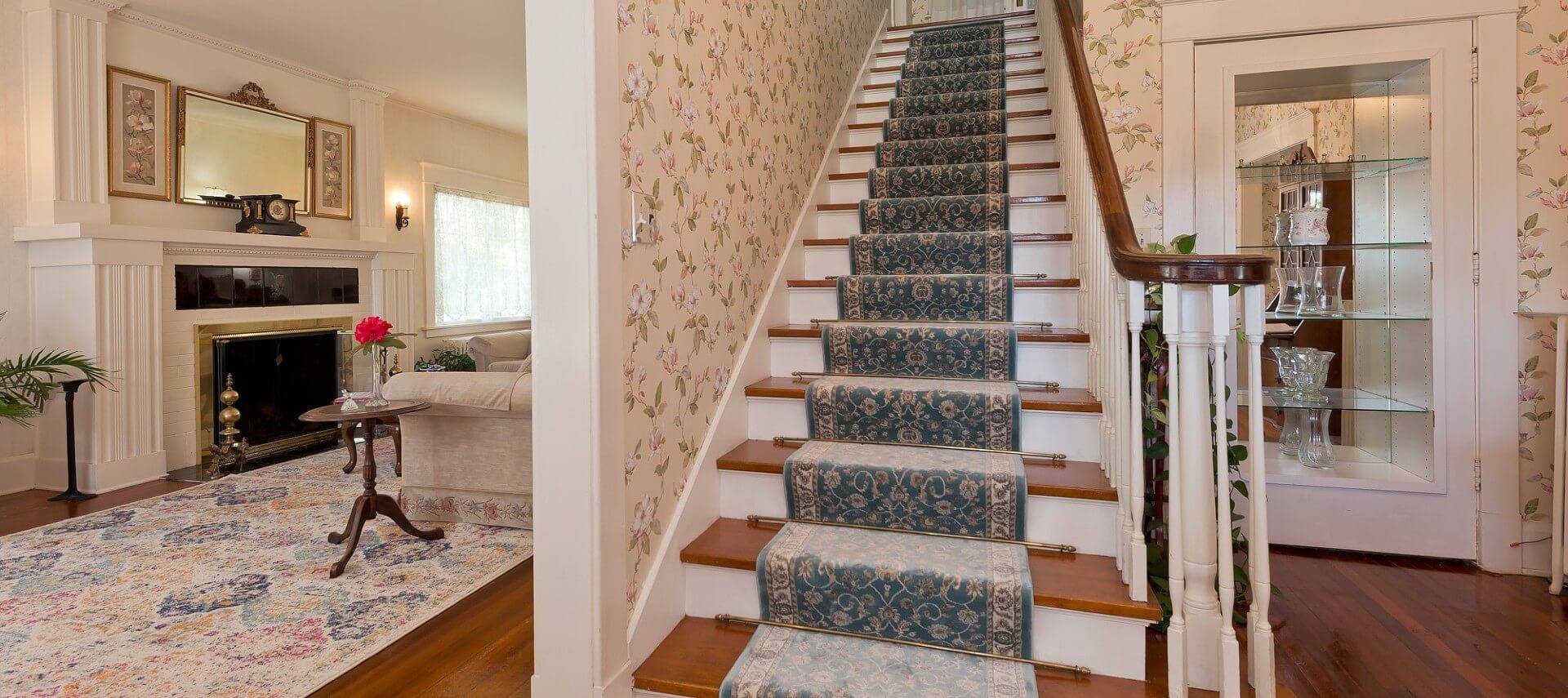 Front entry of a home with stairway upstairs and doorway into living room with couch and fireplace